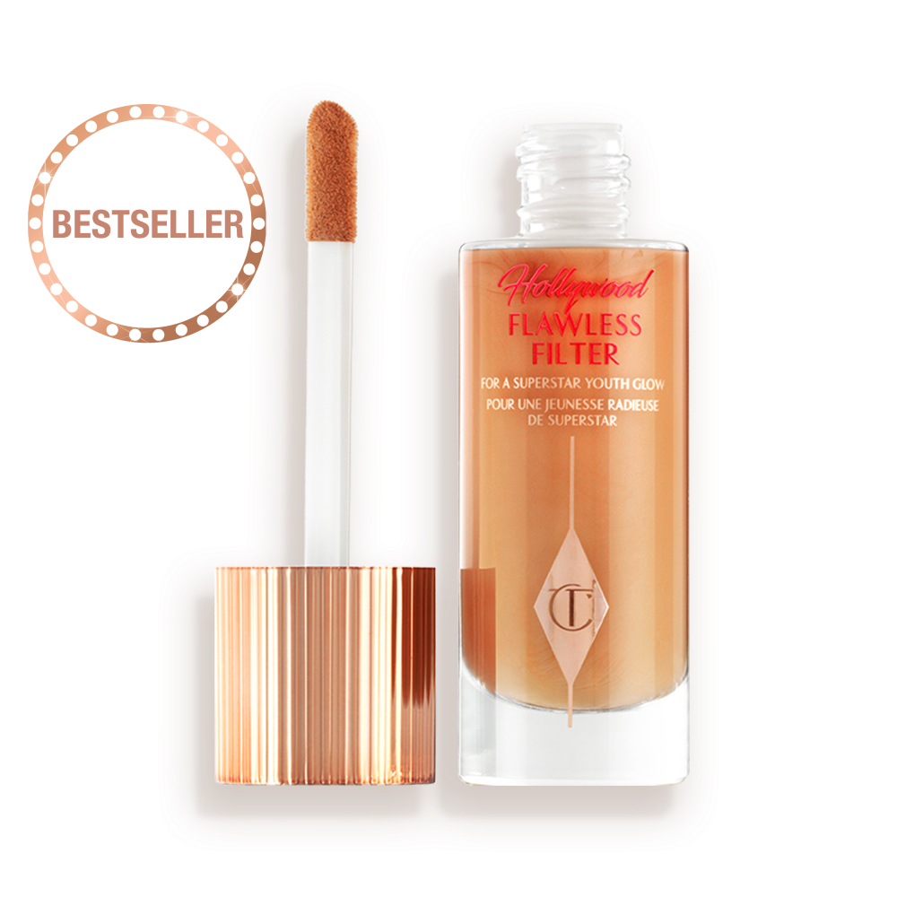 An open, luminous primer in a medium golden-beige shade in a glass bottle with its gold and white doe-foot applicator next to it.
