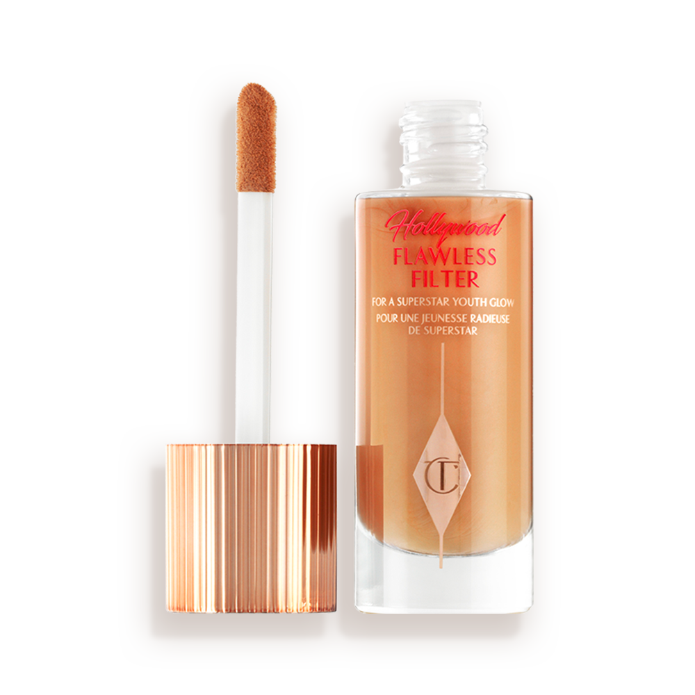 Ein leuchtender Primer in einem mittlerem Gold-Beigeton in einer geöffneten Glasflasche mit seinem angeschrägten Applikator in Gold und Weiß neben sich.