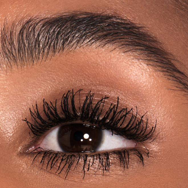 Single-eye close-up of a deep-tone model with brown eyes wearing jet-black lengthening mascara. 