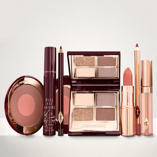 An open two-tone blush in cool-toned brown and warm pink with a mascara, eyeliner pencil, quad eyeshadow palette with shimmery and matte brown and golden shades, an open lipstick in warm pink, lip liner pencil in maroon, and a lip gloss in nude pink. 