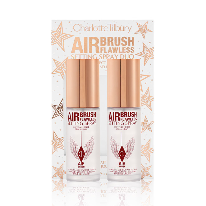 Two, identical, mini setting sprays with gold-coloured lids and their white and gold-coloured packaging box behind them with gold stars printed all over with text on the box that reads, 'Charlotte Tilbury. Airbrush Flawless Setting Spray duo'