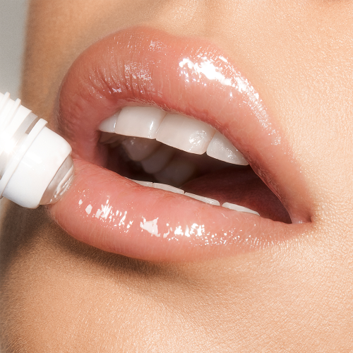 Close-up of a light-tone model applying a nourishing, clear lip oil with a crystal roller ball applicator. 