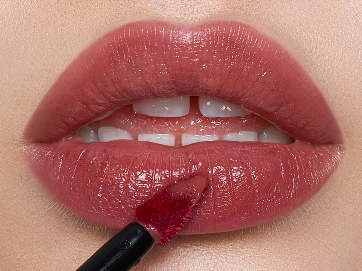 Lips close-up of a light-tone model applying a soft, nude pink lip tint with a doe-foot brush applicator. 