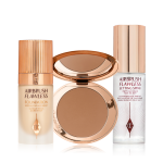 A foundation in a glass bottle with a gold-coloured lid, bronzer compact in a medium-brown shade, and setting spray with a gold-coloured lid. 