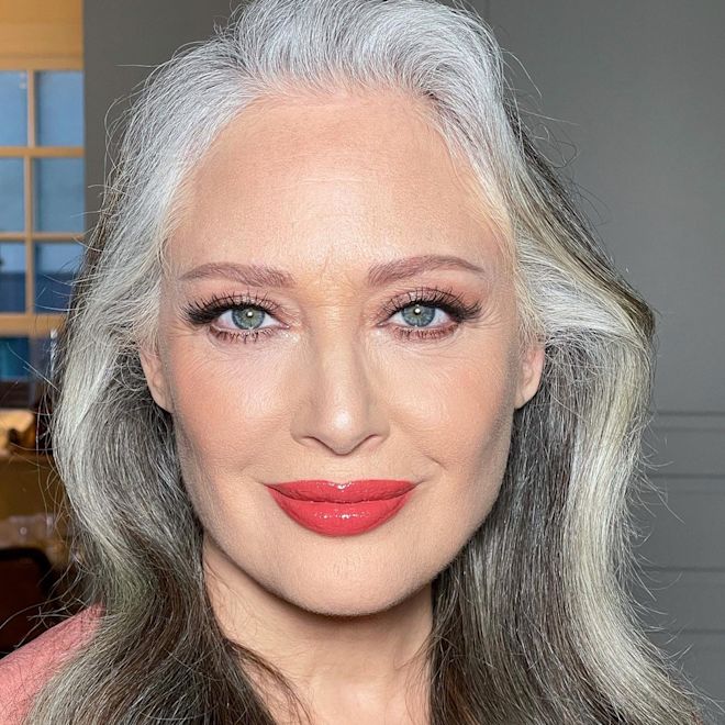 Hyaluronic Happikiss in Happicoral light-tone model Light-tone model with blue eyes and mature skin wearing a high-shine lipstick balm in a deep coral shade.