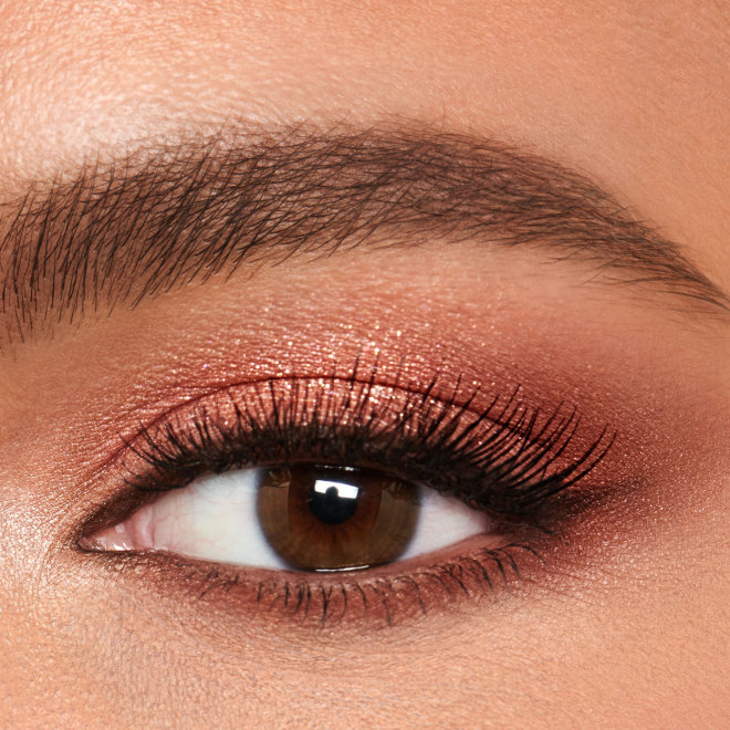 Einzelne Nahaufnahme des Auges eines Models mit mittlerem Hautton und braunen Augen, das ein Augen-Make-up in Perlmutt-Roségold, Altrosa, Beerenbraun und Rosenknospenrosa trägt. 