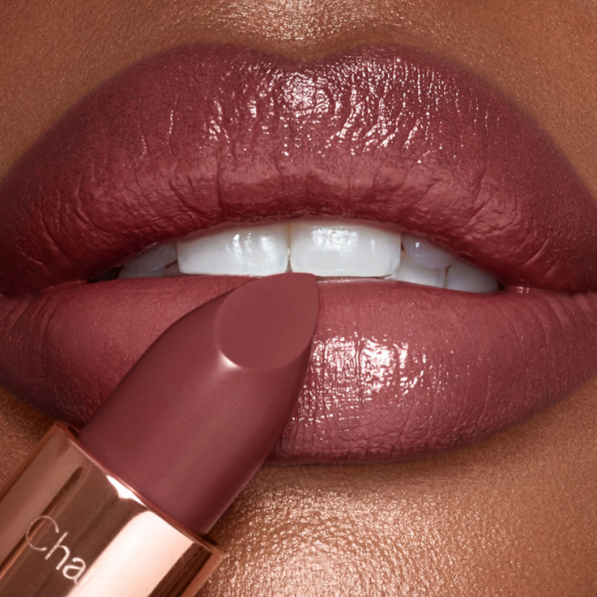 Primer plano de los labios de una modelo de piel oscura aplicándose un labial berry-brown de acabado satinado. 