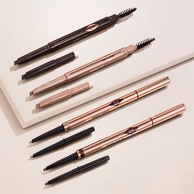 A collection of double-ended eyebrow pencils and eyebrow brushes in shades of black, black-brown, light brown, medium brown, soft brown, dark brown, taupe, and light blonde along with eyebrow tints, all in sleek, gold-coloured packaging.