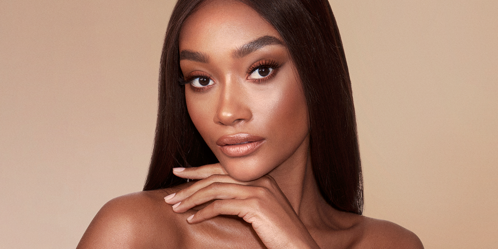 A deep-tone brunette model wearing glowy, nude makeup with bronzed skin. 