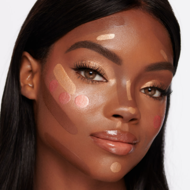 Deep-tone brunette model with unblended contour, medium-pink glowy blush, and an extremely glowy, champagne-coloured highlighter on her face. 