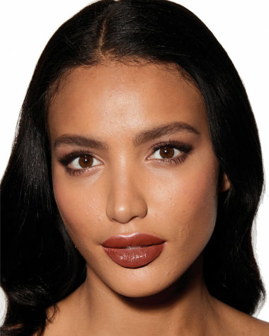 Deep-tone model with brown eyes wearing a moisturising lipstick balm in a soft brown shade with a high-shine finish.