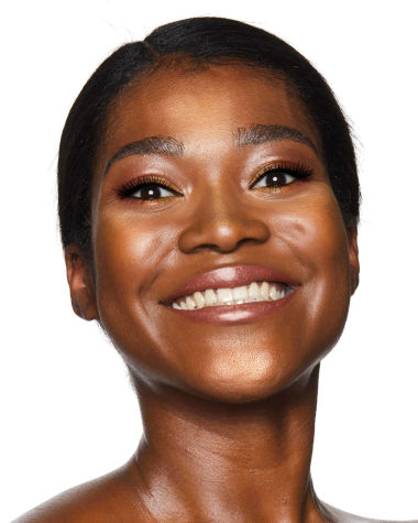 A deep-tone model with brown eyes wearing shimmery copper and gold eye makeup with black eyeliner, glowy bronzed cheeks, and pinkish-brown lipstick with gloss on top. 
