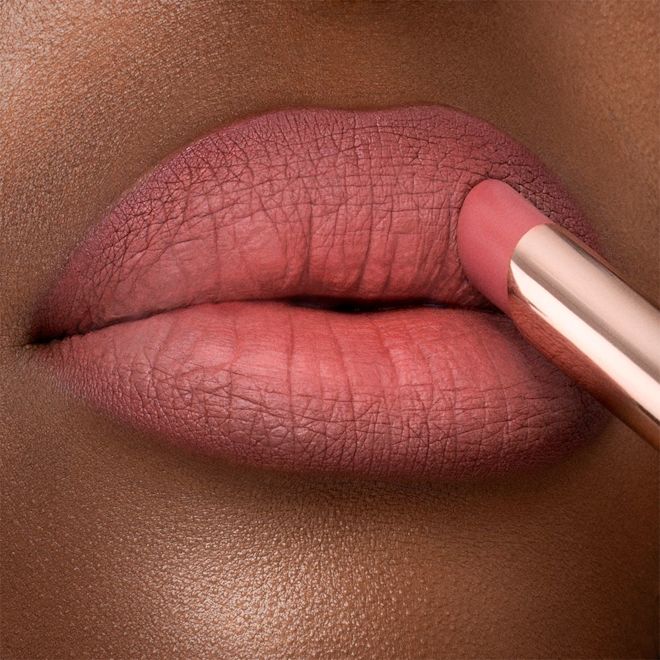 Limitless Lucky Lips in Rose Hope on deep-tone lips close-up Lips close-up of a deep-tone model applying a neutral rosy-pink lipstick with a matte finish.