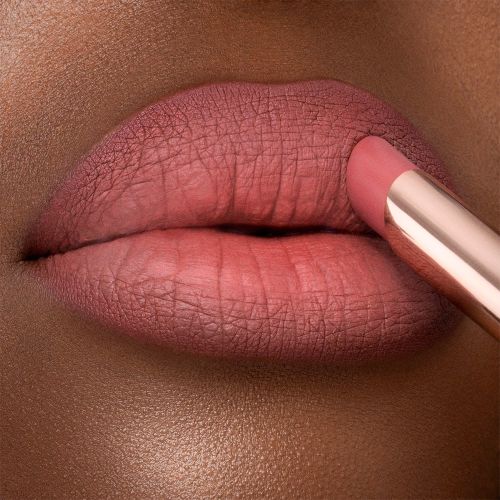 Lips close-up of a deep-tone model applying a neutral rosy-pink lipstick with a matte finish. 