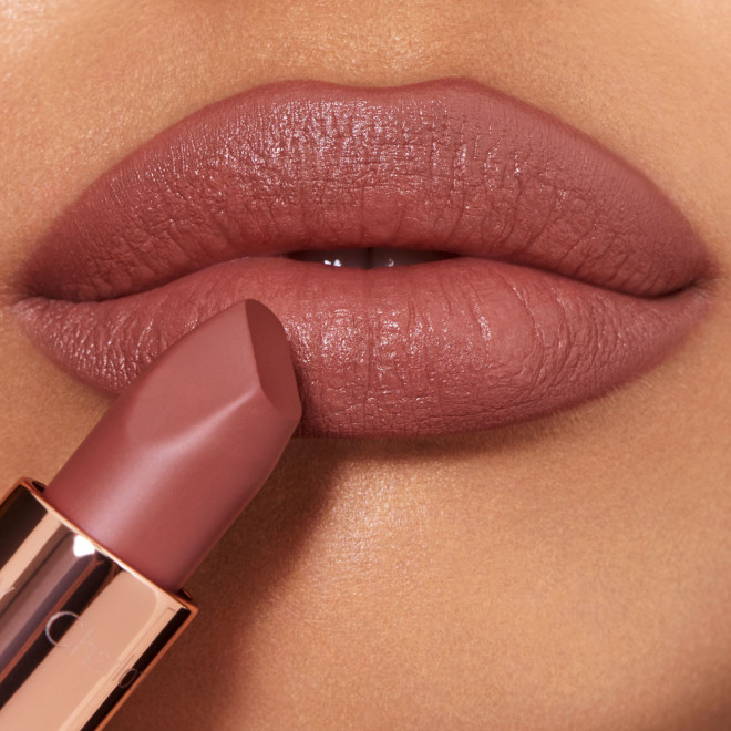Lips closeup of a medium-tone model applying a mid-toned muted nude-rose matte lipstick.

