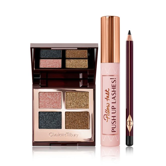 An open, mirrored-lid quad eyeshadow palette in shimmery pink, blue, and gold shades with a mascara with a nude pink tube and gold-coloured lid, and an eyeliner pencil in a black shade with a dark crimson body. 