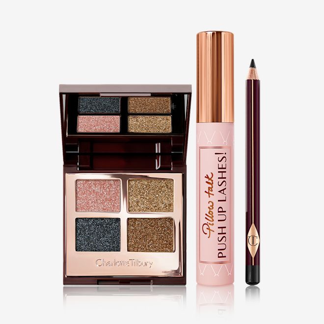 Party Eye Kit displayed. An open, mirrored-lid quad eyeshadow palette in shimmery pink, blue, and gold shades with a mascara with a nude pink tube and gold-coloured lid, and an eyeliner pencil in a black shade with a dark crimson body.