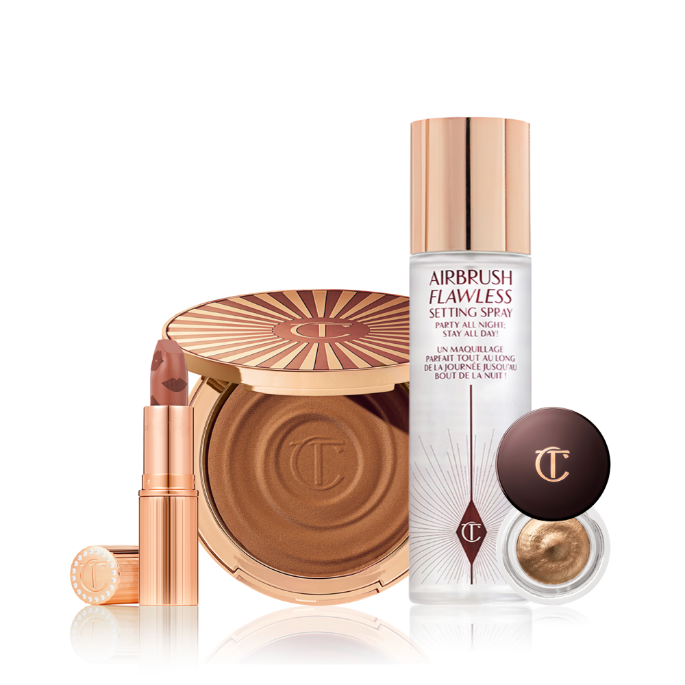 An open nude peach lipstick in a golden-coloured tube, cream bronzer compact with a mirrored lid, setting spray with a gold-coloured lid, and cream eyeshadow in a a glass pot with a dark brown coloured lid.