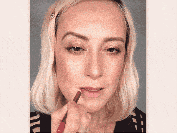 GIF of a light-tone blonde makeup artist applying a lip liner with lipstick and putting a gloss on top. 