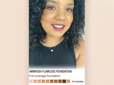A medium-tone model with glowy makeup wearing magenta lipstick and light blush with glowy matte foundation with the option to try on the foundation yourself virtually in different shades, which are all displayed on the screen. 