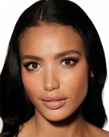 Deep-tone model with brown eyes wearing a pale pink matte lipstick with shimmery terracotta eyeshadow, rosy peach blush, and dark glowy bronzer. 