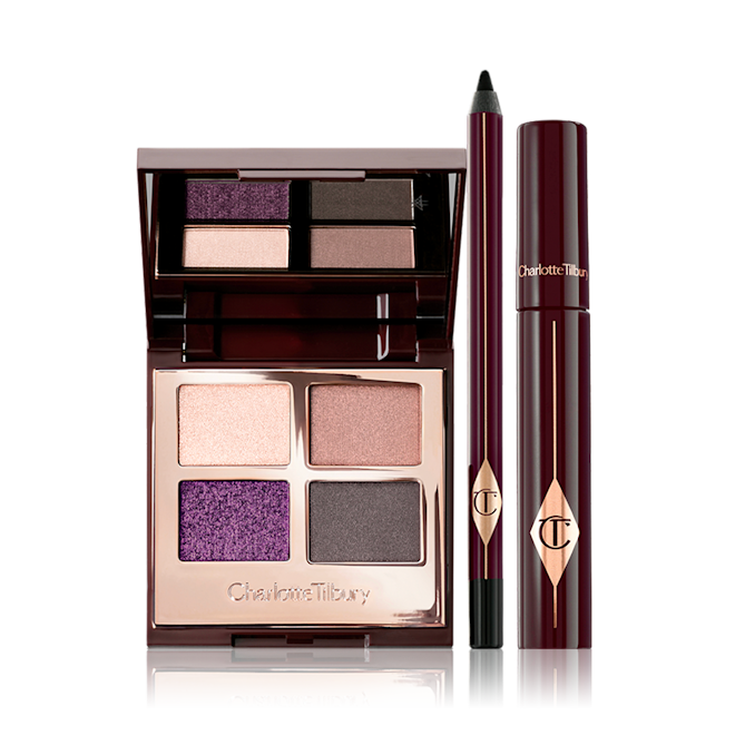 Glamour Muse Kit displayed An open, mirrored-lid eyeshadow palette with eyeshadows in shades of purple, gold, and grey, an eyeliner pencil in black, and a black mascara in dark crimson packaging.