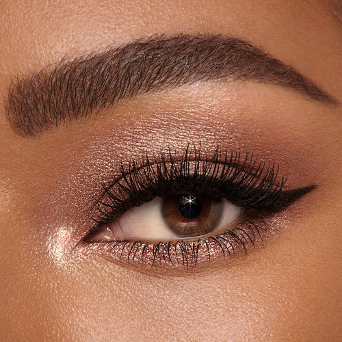 Single-eye close-up of a deep-tone model with brown eyes wearing shimmery bronze, brown, and gold eye makeup.