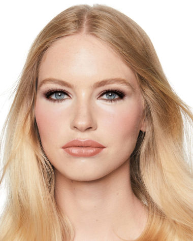 A fair-tone model with blue eyes wearing smokey brown eye makeup with muted pink blush with glossy soft-brown lips.