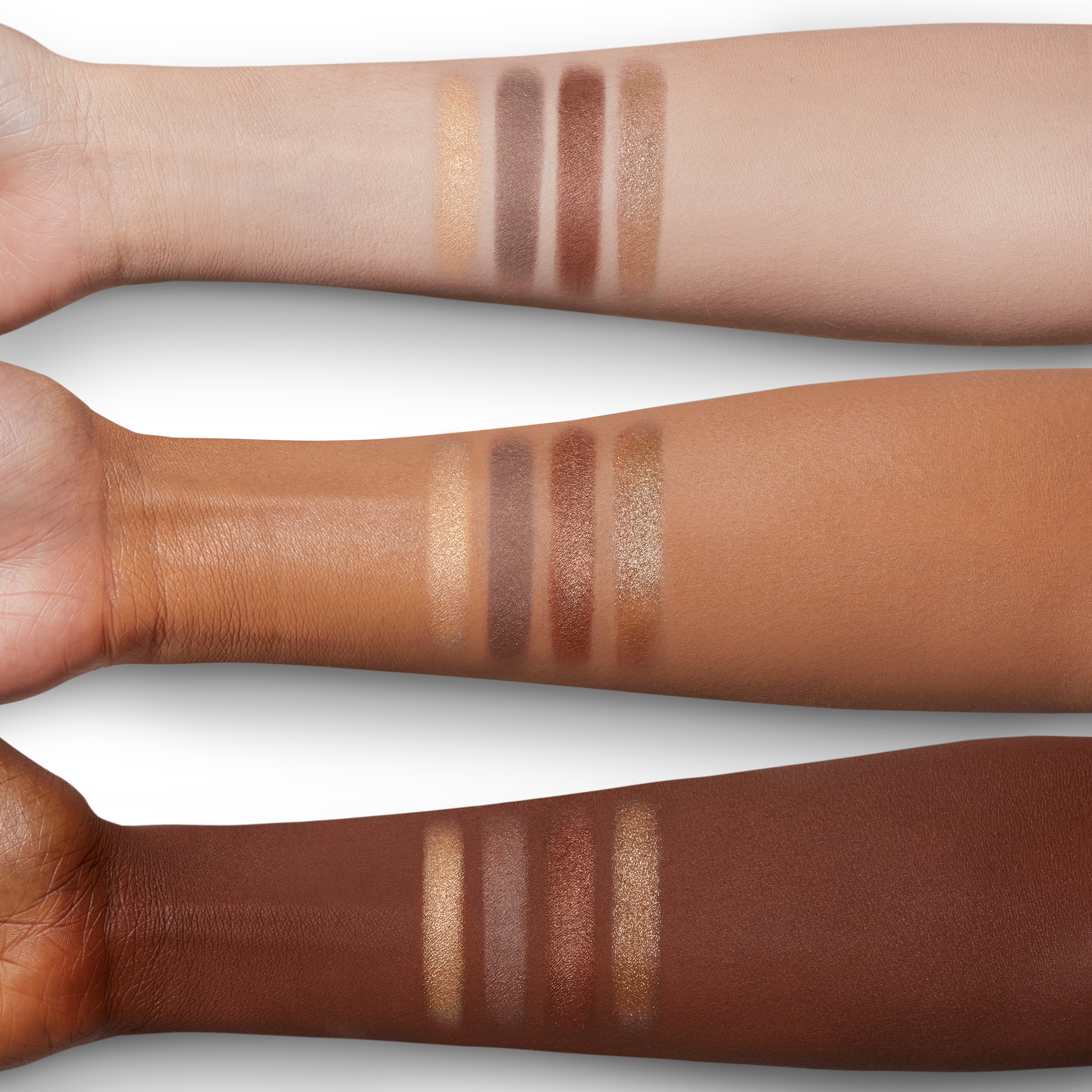 Arm swatches of four shimmery eyeshadows in champagne, bronze, and smokey grey colours on fair, tan, and deep skin. 