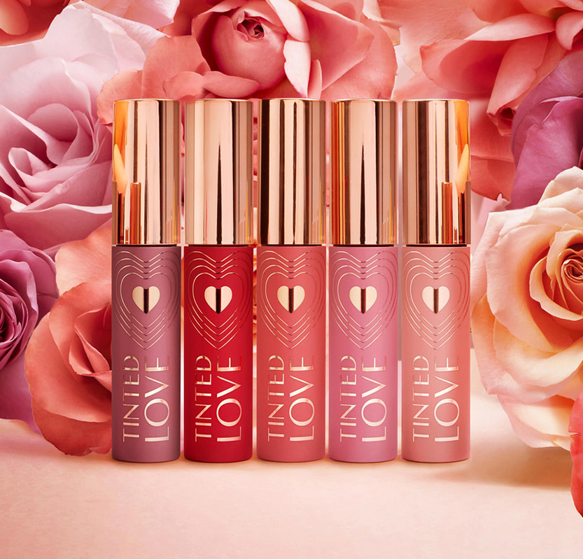 Five, closed lip and cheek tints in purple, red, coral, pink, and peach-coloured tubes with gold-coloured lids.