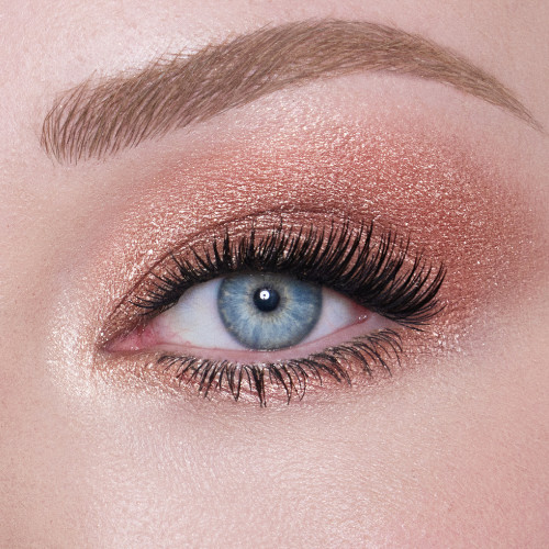 Single-eye close-up of a fair-tone model with blue eyes wearing an iridescent rose gold eyeshadow with very fine shimmer. 