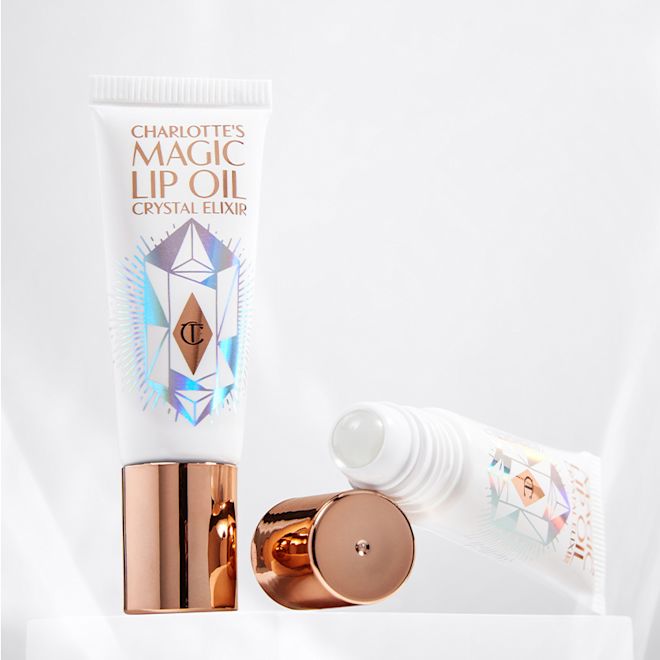 Charlottes Magic Lip Oil with and without lid Two lip oils, with and without lids, in white and rose gold packaging with shimmery geometric shapes on the tube.