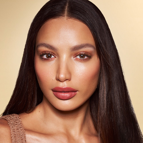 medium-tone brunette model with brown eyes wearing sunset, sultry-pink eyeshadow, soft pink blush and lip stain, and dewy opal-coloured highlighter for a sun-kissed, glowing makeup look.