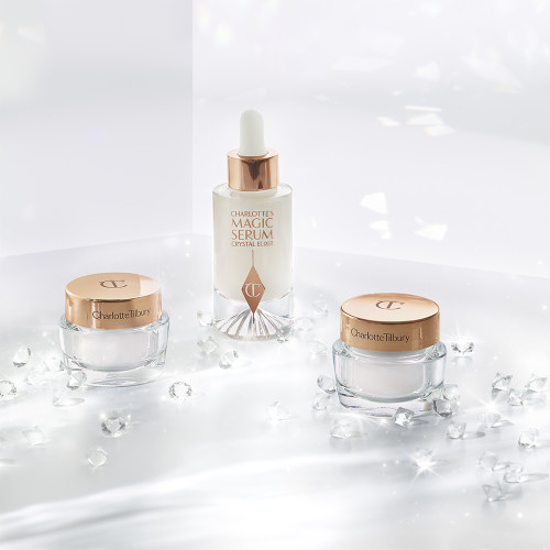 Travel-size, pearly-white face cream in a glass jar with a gold-coloured lid, travel-size fawn-coloured night cream in a glass jar with a gold-coloured lid, and luminous face serum in a glass bottle with a white and gold dropper lid.