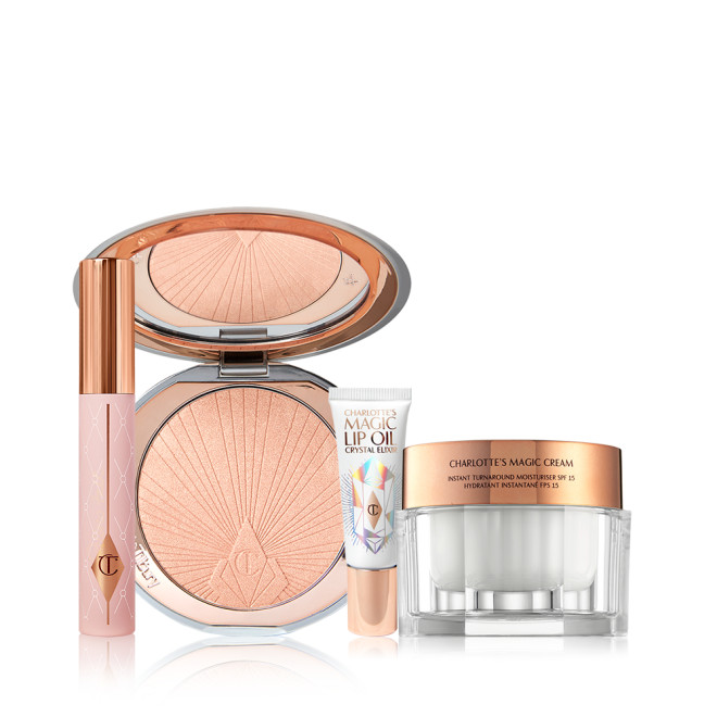 Open highlighter compact in a rose gold shade with a mirrored lid, pearly-white face cream in a glass jar with a gold-coloured lid, black-coloured mascara in a nude pink tube with a gold-coloured lid, and lip oil in a white-coloured tube with gold-coloured lid.
