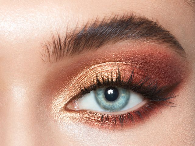 Close-up of a light-tone model's blue eye with shimmery gold, rust, and brown eye makeup. 