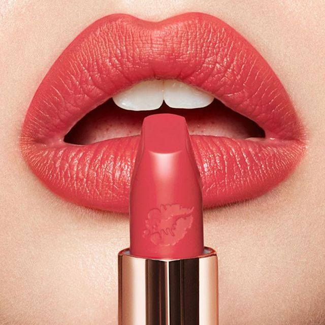 Lips close-up of a fair-tone model wearing a strawberry red matte lipstick while holding the lipstick in front of her lips.