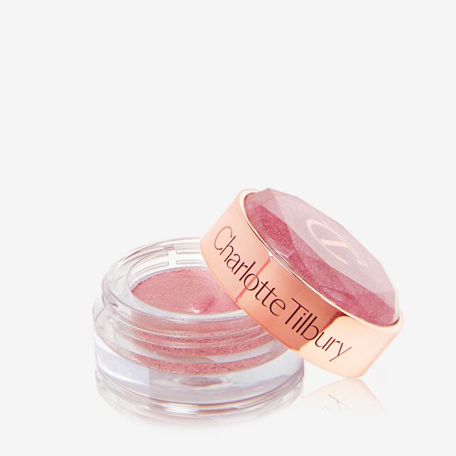 Jewel Pot in Pillow Talk open A shimmery eyeshadow pigment in a rose gold shade in a glass pot with its lid next to it.