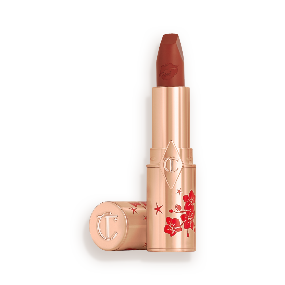 A matte burnt-orange red lipstick in gold-coloured packaging with cherry blossoms illustrated on the tube for the Lunar New Year, along with its lid next to it.