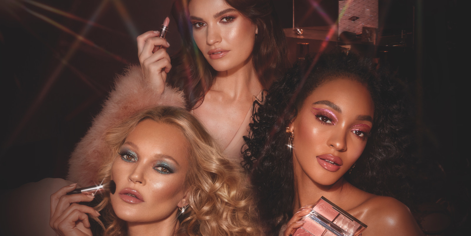 Banner with a model trio wearing glittery eye makeup in bright shades with matte lipsticks in nude colours.