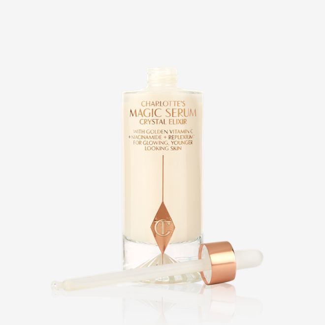 Charlotte's Magic Serum Crystal Elixir open An open luminous, ivory-coloured serum in an opened glass bottle with its dropper beside it.
