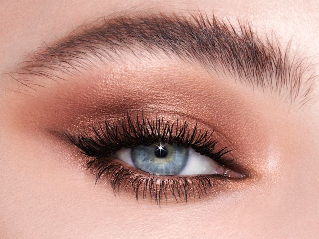 Single-eye close-up of a fair-tone model with blue eyes wearing shimmery brown and gold eyeshadow. 