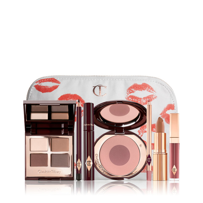 A makeup bag with 7 makeup products, which are a quad eyeshadow palette in shades of champagne, gold, and bronze, a dark brown eyeliner pencil, mascara, a two-tone brown and pink powder blush, tawny-brown lip liner, a terracotta lipstick, and a deep pinkish-red lip gloss. 