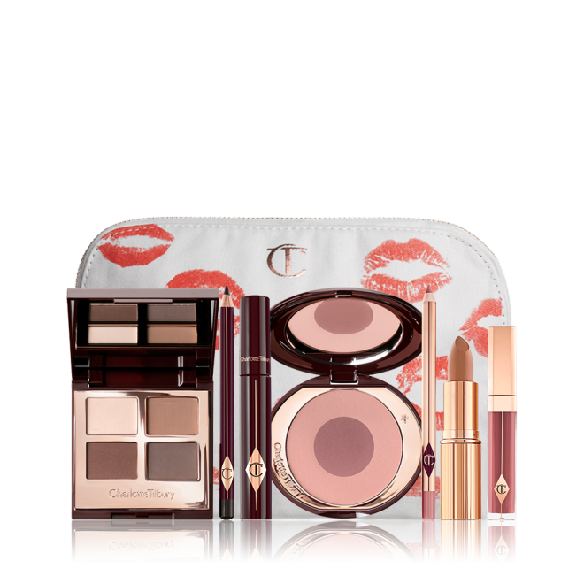 A makeup bag with 7 makeup products, which are a quad eyeshadow palette in shades of champagne, gold, and bronze, a dark brown eyeliner pencil, mascara, a two-tone brown and pink powder blush, tawny-brown lip liner, a terracotta lipstick, and a deep pinkish-red lip gloss. 