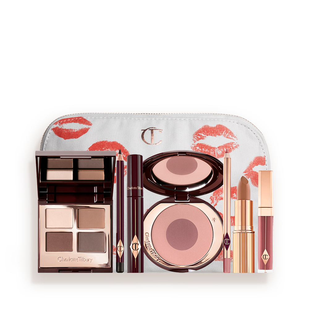 A makeup bag with 7 makeup products, which are a quad eyeshadow palette in shades of champagne, gold, and bronze, a dark brown eyeliner pencil, mascara, a two-tone brown and pink powder blush, tawny-brown lip liner, a terracotta lipstick, and a deep pinkish-red lip gloss. 