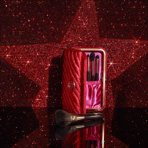 An open, bright-red-coloured velvet brush clutch with the iconic CT logo on the front in gold and travel-sized makeup brushes inside.