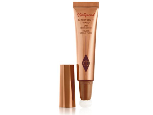 Un highlighter líquido abierto en formato wand en un tono rose-gold dreamy, con un tubo color marrón cobrizo, un aplicador suave tipo esponja en la punta y la tapa al lado.