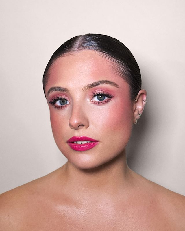 Close-up of a fair-tone model with blue eyes wearing magenta matte lipstick with berry rose and brown dramatic eye makeup with berry rose blush.