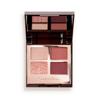 An open, mirrored-lid eyeshadow palette in shades of rose gold, champagne, maroon, and redwood. 