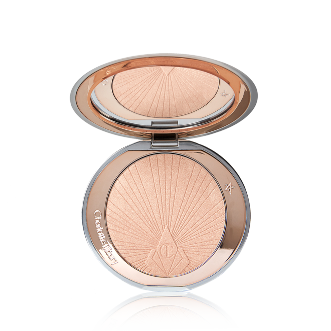  An open, pressed powder highlighter compact in a light pinky beige shade with a mirrored lid. 